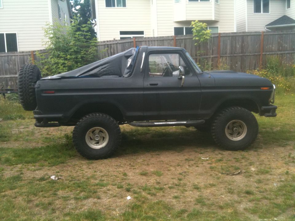Side view of a black 1979 Ford Bronco with a spare tire on the rear and a tarp over the bed