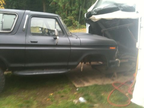 1979 Ford Bronco - A matte black Ford Bronco is partially covered by a tarp, suggesting it is undergoing repairs or storage.