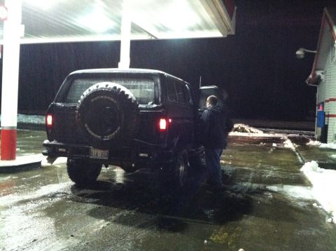 1979 Ford Bronco - A person stands by the open driver's door of a black Ford Bronco at a gas station in the snow.