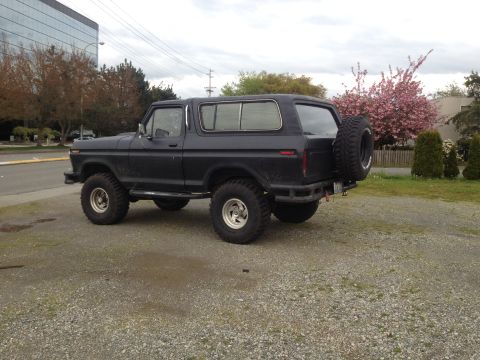 1979 Ford Bronco - Dark SUV parked on gravel with a spare tire on the rear.