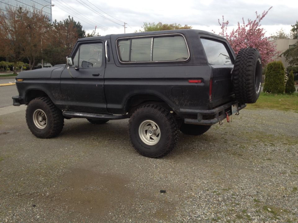 Black Ford Bronco with a spare tire mounted on the rear, parked on a gravel lot