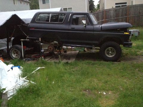 1979 Ford Bronco - Ford Bronco is lifted and undergoing repairs in a grassy yard.