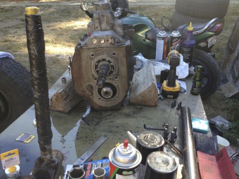1979 Ford Bronco - Various automotive parts, including a transmission and driveshaft, are spread out on a table with a motorcycle visible in the background.