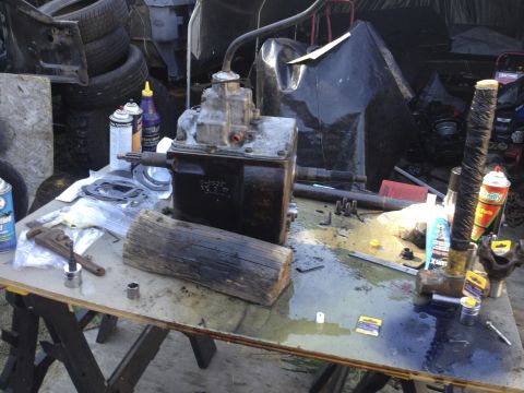 1979 Ford Bronco - A transmission part sits on a workbench surrounded by tools and various automotive fluids.
