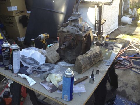 1979 Ford Bronco - Workbench setup with a transmission, gaskets, tools, and cleaning supplies, suggesting a repair or rebuild process.
