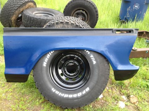 1979 Ford Bronco - A blue truck bed panel is shown with a tire. Other tires and a trash can are visible in the background.