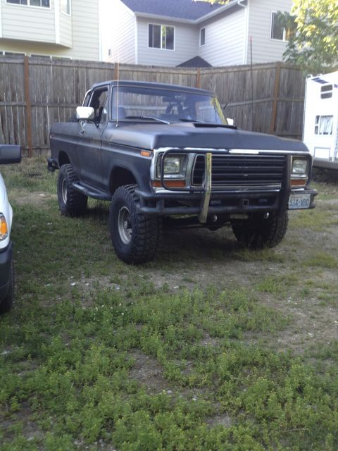 1979 Ford Bronco - This lifted Ford F-Series truck is parked in a grassy yard with houses and a fence in the background.