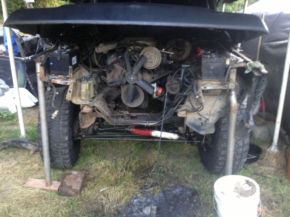 Black vehicle engine bay with exposed engine, radiator, and suspension components. Tires visible