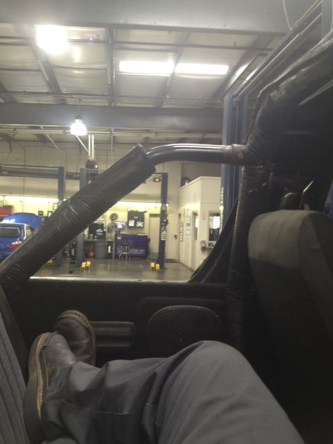 1979 Ford Bronco - A person's legs and feet are visible inside a vehicle, with a workshop in the background.