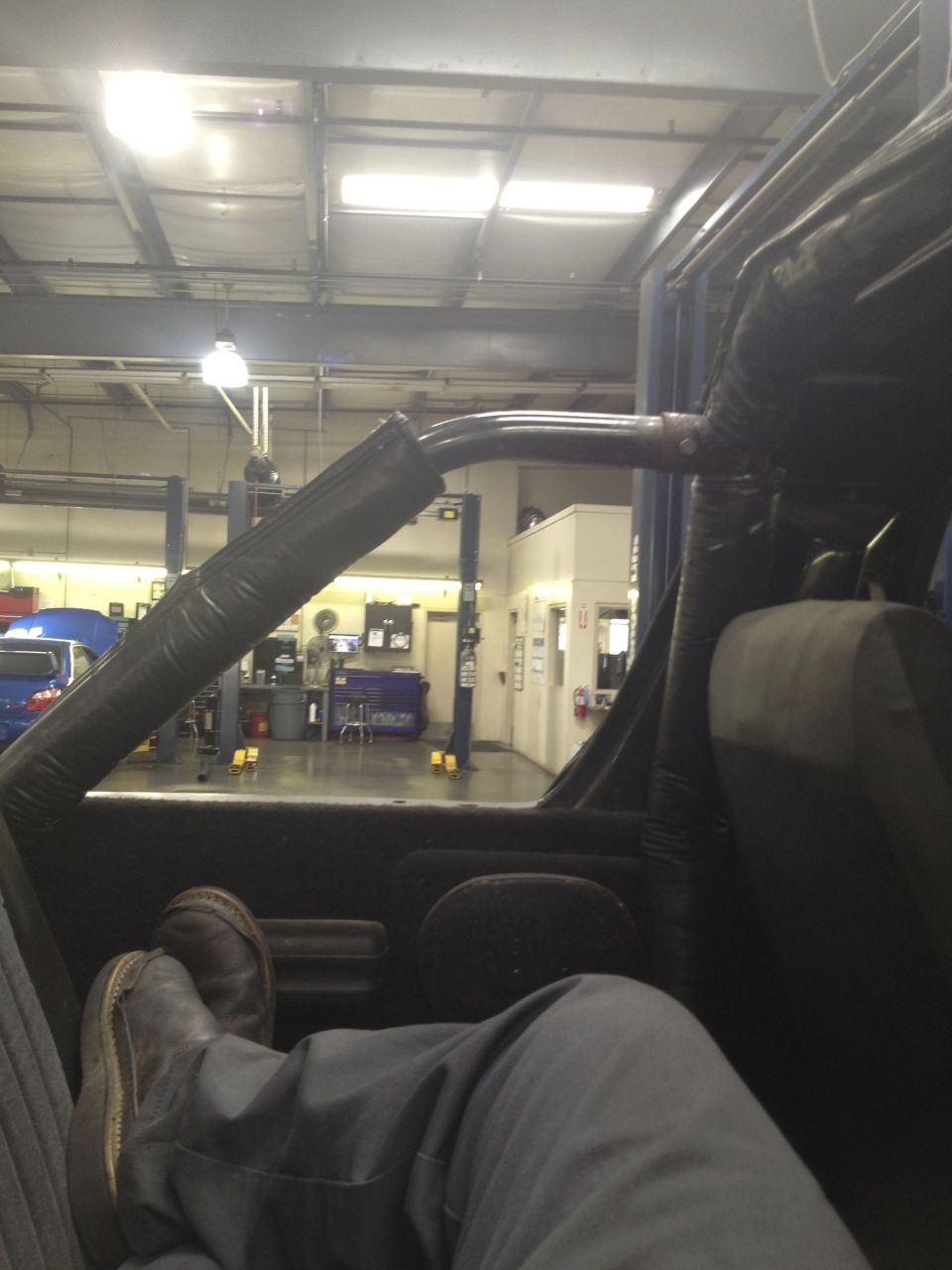 Interior view of a vehicle with padded roll bar and a person's legs and feet visible