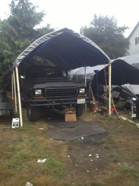 1979 Ford Bronco - A black 1979 Ford Bronco is parked under a temporary shelter, showing its front grille and license plate.
