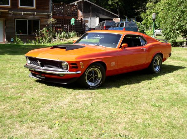 Orange 1970 Ford Mustang Boss 429 parked on grass in front of a wooden house