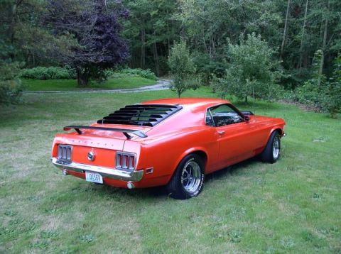 1979 Ford Bronco - Rear three-quarter view of an orange 1970 Ford Mustang coupe with a spoiler and rear window louvers.