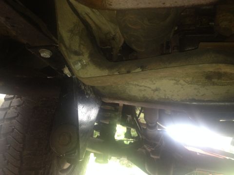 1979 Ford Bronco - Underside view of a vehicle's chassis and suspension components, with a tire visible on the left.
