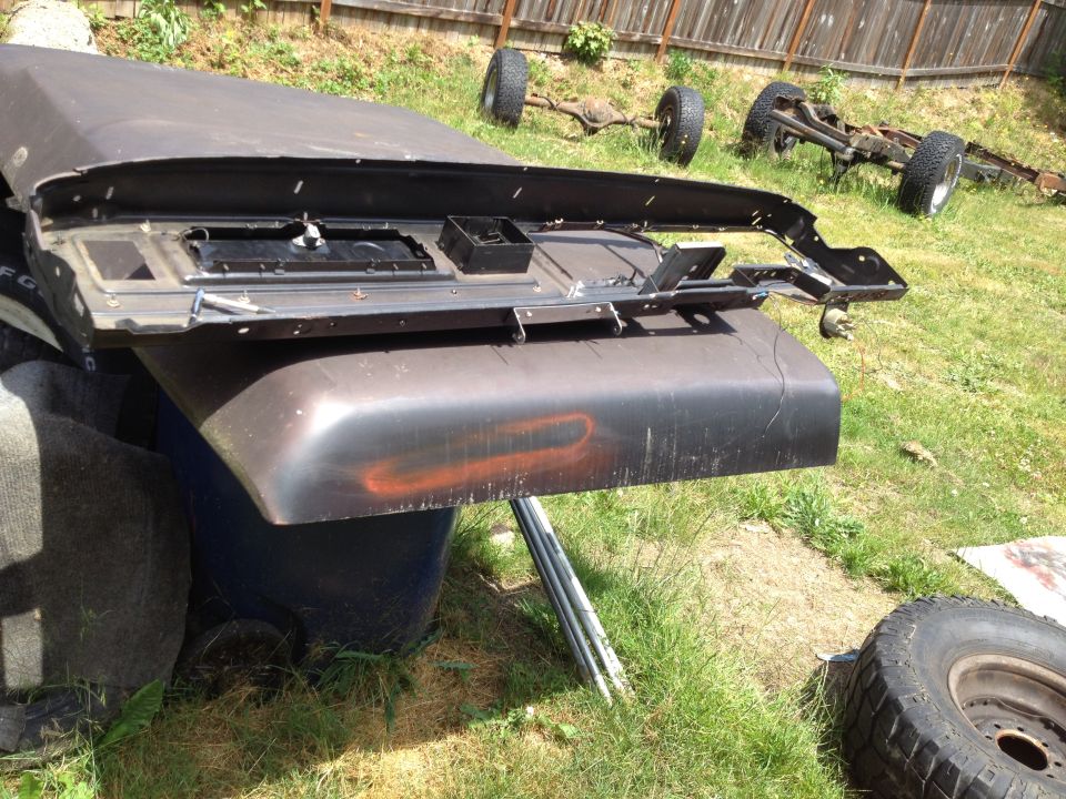 Dark car part resting on a blue trash can outdoors