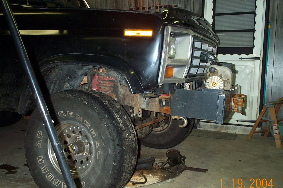 Front corner of a black Ford pickup or Bronco on jack stands with a winch bumper in a garage
