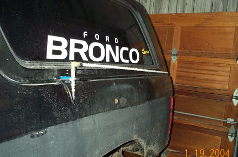 1986 Ford Bronco - A black Ford Bronco is parked inside a garage with a wooden door.