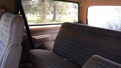 1984 Ford Bronco - Interior view of a vintage SUV with plaid seats and a roll bar, seen from the rear.