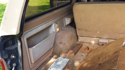 1984 Ford Bronco - The interior of this SUV shows a tan door panel and rear seat, with debris scattered in the cargo area.
