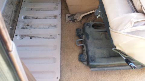 1984 Ford Bronco - Close-up of the interior floor and seat base, showing metal components and carpeting.