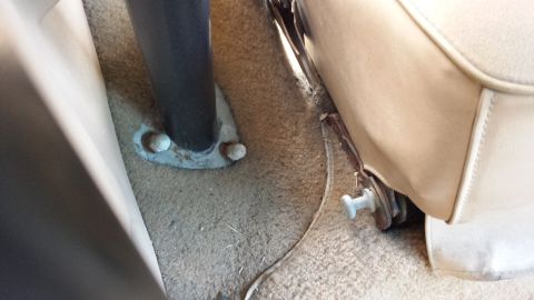 1984 Ford Bronco - The interior of the vehicle shows the floor carpet and the base of a seat with a metal support post.