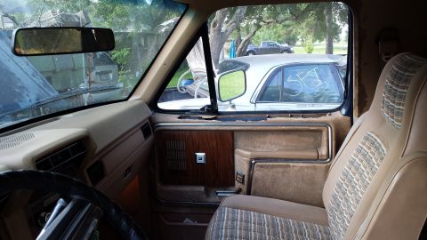 1984 Ford Bronco - Interior view of a tan truck, showing the door panel and seat, with another vehicle visible outside.