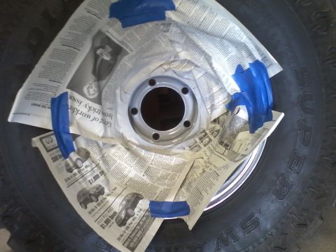 1978 Ford Bronco - A wheel rim is being prepped for painting, covered with newspaper and secured with blue tape.