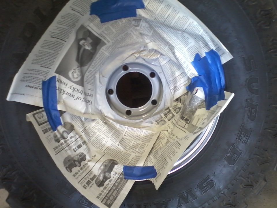 Wheel rim covered in newspaper and blue tape, with a tire visible