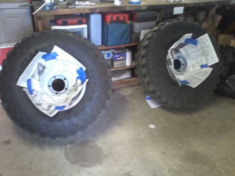 1978 Ford Bronco - Two large off-road tires are prepped for painting, with the rims taped off to protect them.