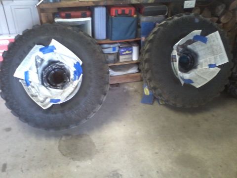 1978 Ford Bronco - Two large tires are prepared for painting, with their hubs covered to protect them from spray.