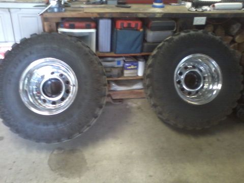 1978 Ford Bronco - Two large off-road tires and chrome wheels are displayed in a workshop.