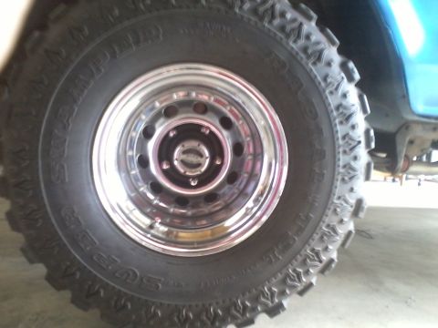 1978 Ford Bronco - Close-up of a chrome wheel and aggressive off-road tire on a blue vehicle.