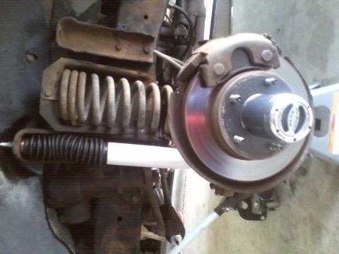 1978 Ford Bronco - Close-up of a vehicle's front suspension system, showing a coil spring, shock absorber, and brake assembly.