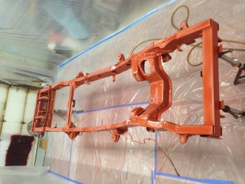 1993 Ford Bronco - A vehicle frame is being painted orange inside a spray booth, covered in plastic sheeting.