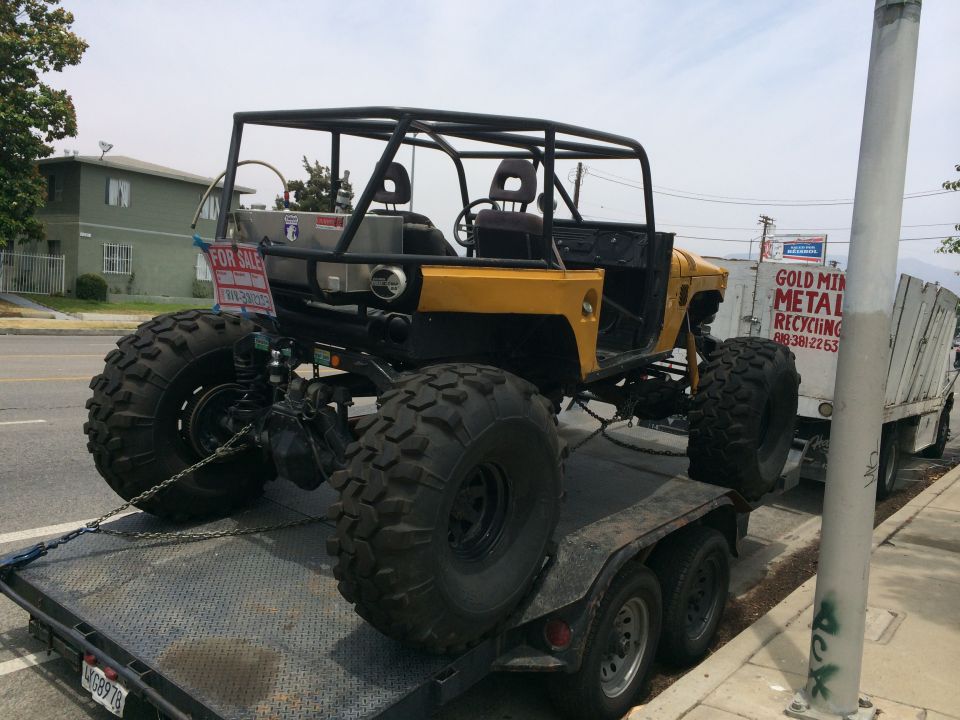 Yellow off-road vehicle with large tires on a trailer, "FOR SALE" sign visible