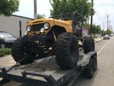 1968 Ford Mustang - A heavily modified yellow off-road vehicle with a roll cage is chained to a trailer.