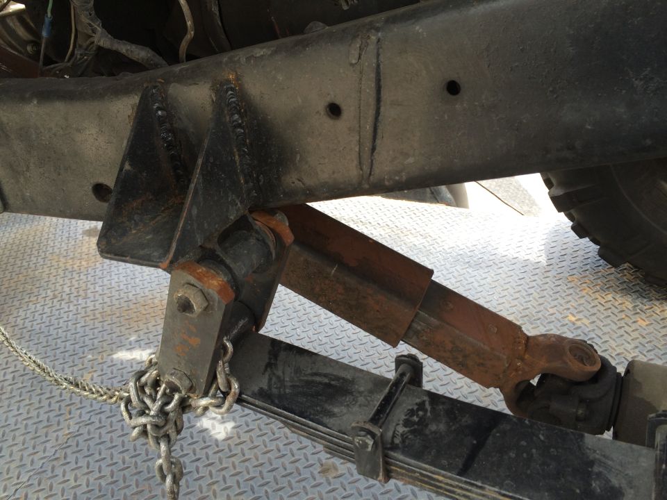 Close-up of a vehicle's rusty driveshaft, leaf spring, and frame with a chain attached