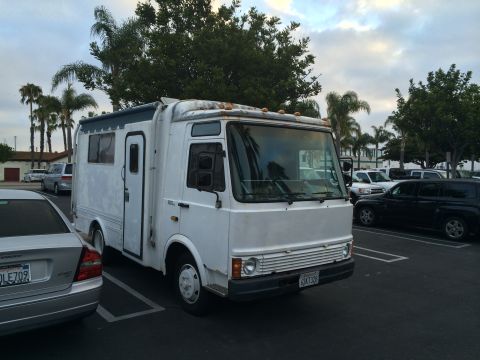 1968 Ford Mustang - A white RV motorhome is parked in a lot with other vehicles and palm trees in the background.