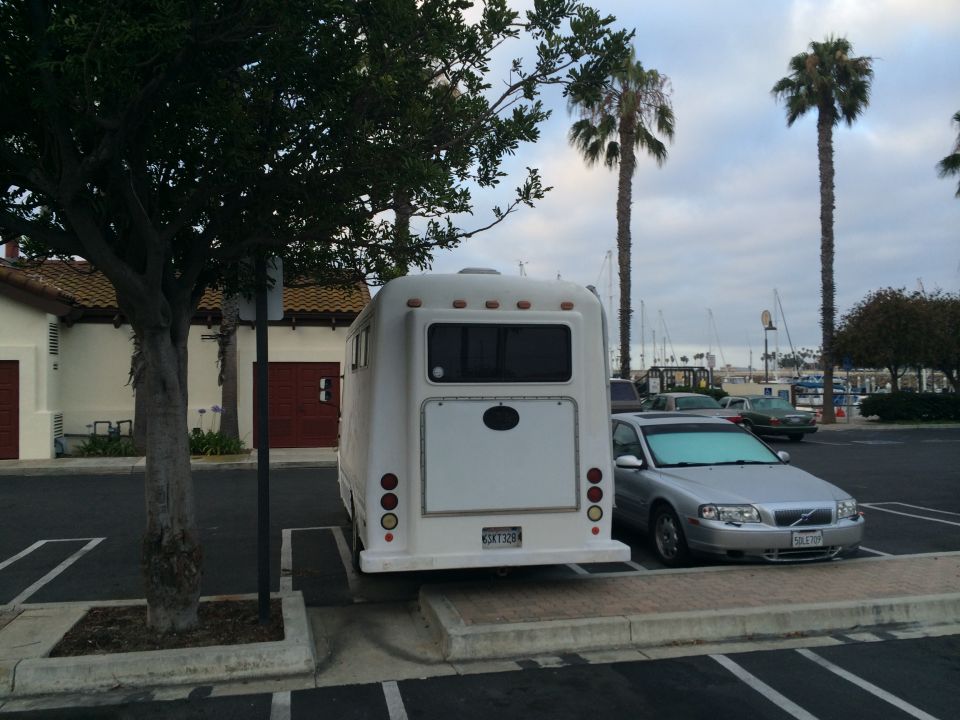 Rear of a white RV parked next to a silver sedan in a parking lot