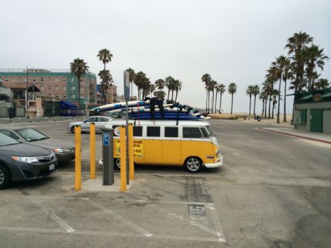 1968 Ford Mustang - A vintage Volkswagen van, equipped for surfing, is parked in a lot with palm trees and buildings in the background.
