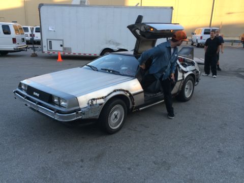1968 Ford Mustang - A DeLorean DMC-12, recognizable by its gullwing doors and stainless steel body, is shown with a person entering.