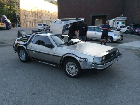 1968 Ford Mustang - A DeLorean DMC-12 is parked outside with its distinctive gullwing doors open.
