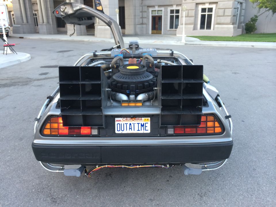Rear view of a DeLorean with its gull-wing doors open, showing the flux capacitor and 'OUTATIME' license plate