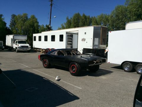 1968 Ford Mustang - Modified 1969 Dodge Charger, likely for a film production, sits in a parking lot with trailers.