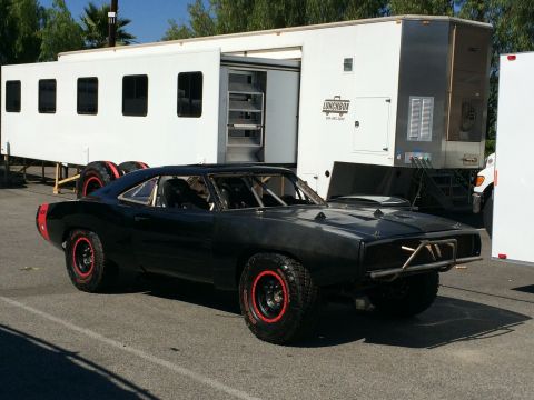 1968 Ford Mustang - Modified black Dodge Charger with off-road tires and a roll cage is parked next to a large white trailer.
