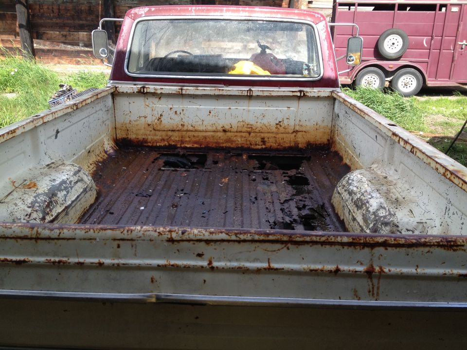Rear view of a red 1974 Ford F-250 pickup truck bed with rust and debris
