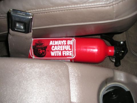 1996 Ford Bronco - A red fire extinguisher Smokey Bear and a safety message is secured between the seats of a vehicle.