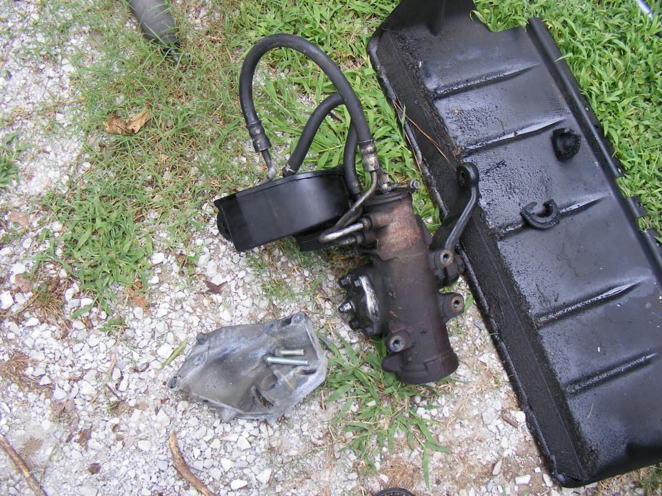 Power steering gearbox with hoses and reservoir, next to a metal bracket