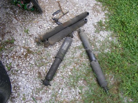 Four used shock absorbers on gravel and grass. One has a label with text