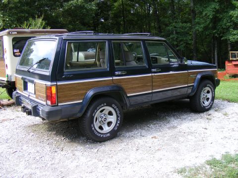 Dark blue Jeep Cherokee XJ with wood paneling parked on gravel
